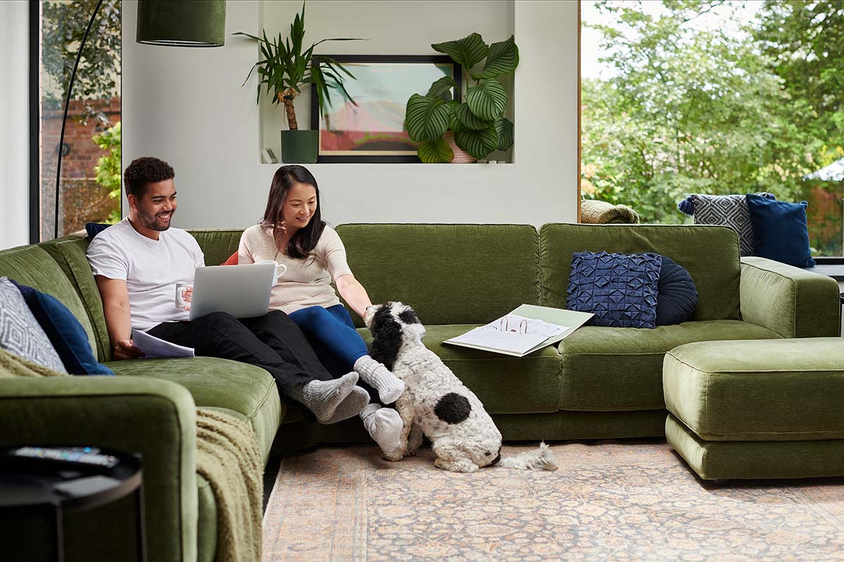 Man and woman sitting on a green couch while petting a dog