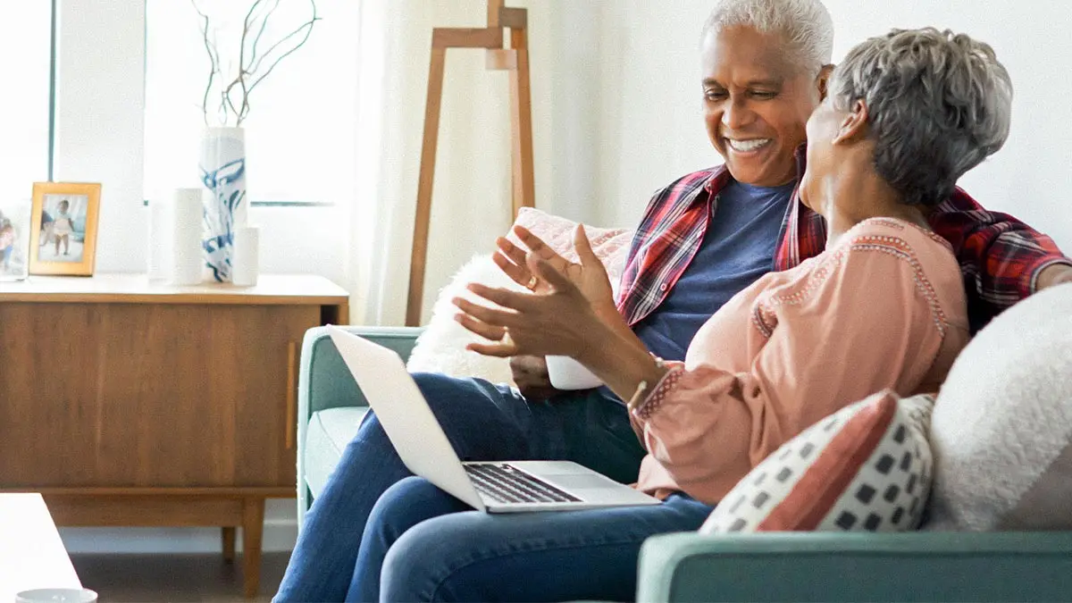 senior copule sitting on their couch reviewing something on their laptop