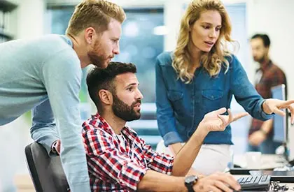 Three co-workers discussing something around a desk.