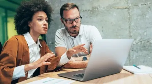 Office colleagues in front of a laptop discussing payment trends for embedded finance for b2b payments.