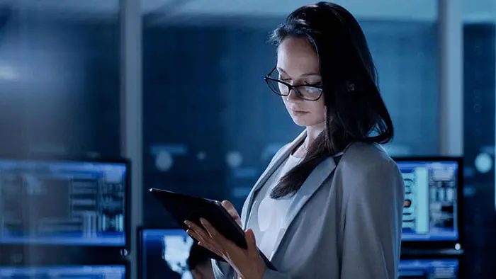 Woman standing in a room with several computers and looking at her tablet device