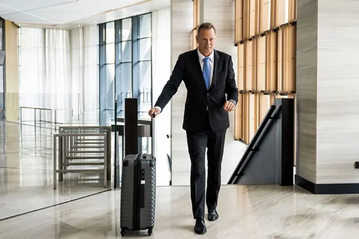 Businessman wearing a suit and wheeling a suitcase into a hotel lobby.