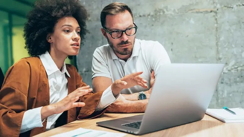 Office colleagues in front of a laptop discussing payment trends for embedded finance for b2b payments.