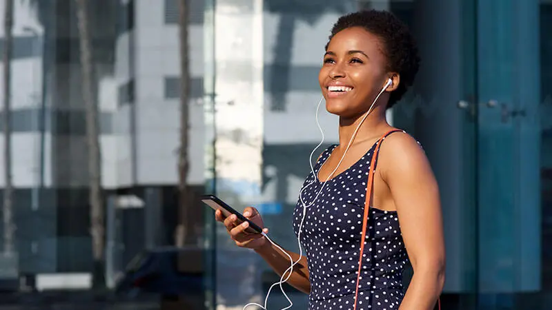 Person smiling holding a smartphone and wearing earbuds, enjoying financial peace of mind