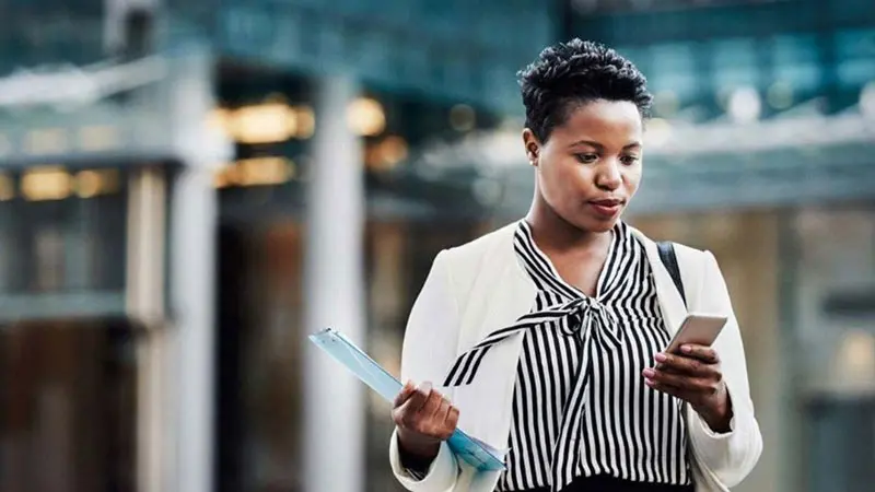 Woman standing outside a commercial building and reading about mutual funds on her phone