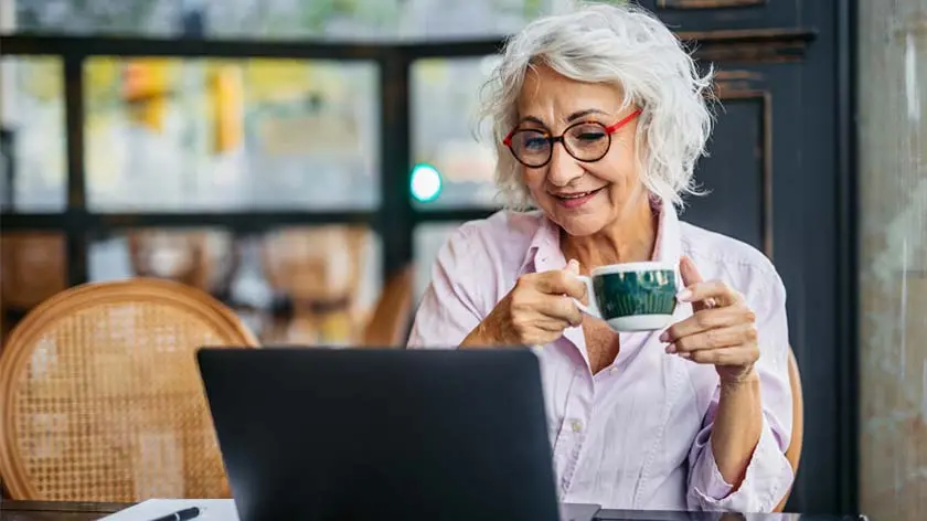 senior woman drinking coffee and looking at her laptop