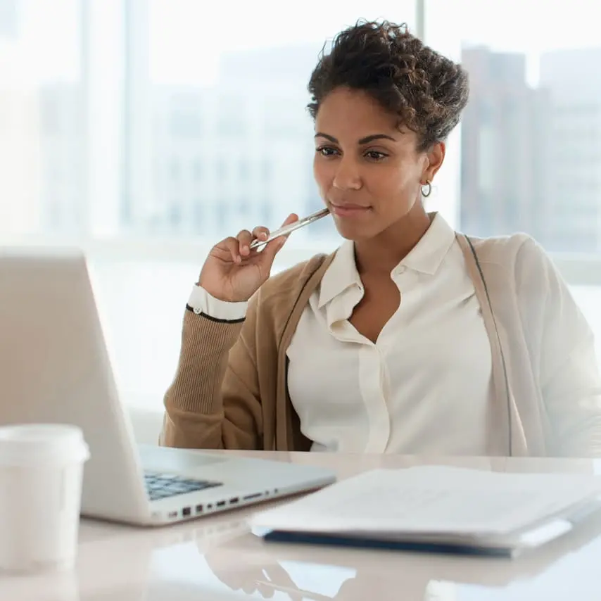 Woman holding pen while sitting and watching a video on her laptop