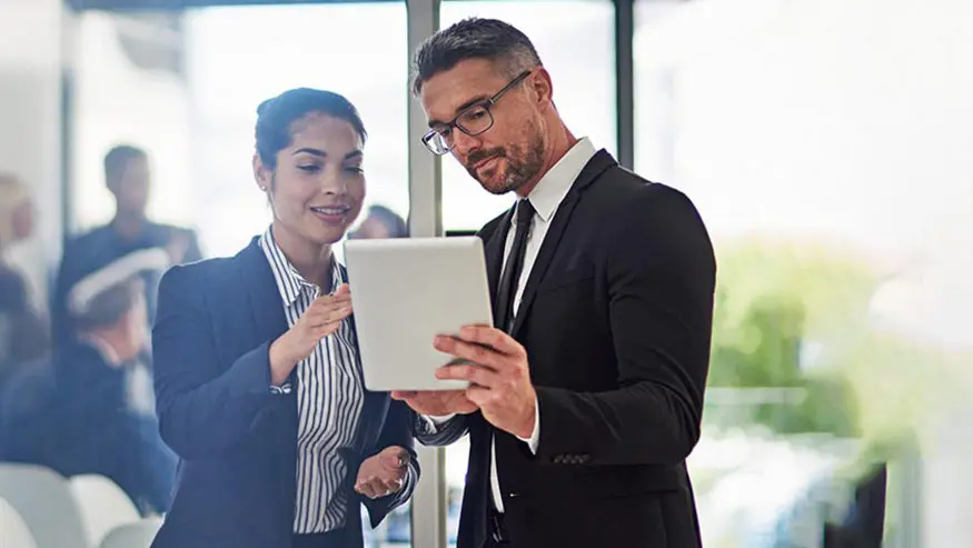 Man and woman in suits looking at a tablet and talking about tax deductions