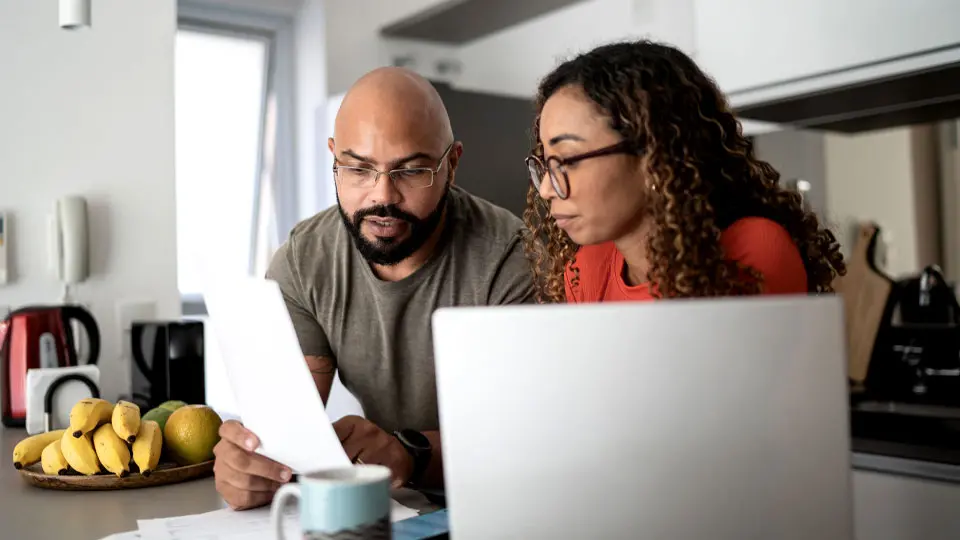 couple reviewing paperwork at their laptop in their kitchen