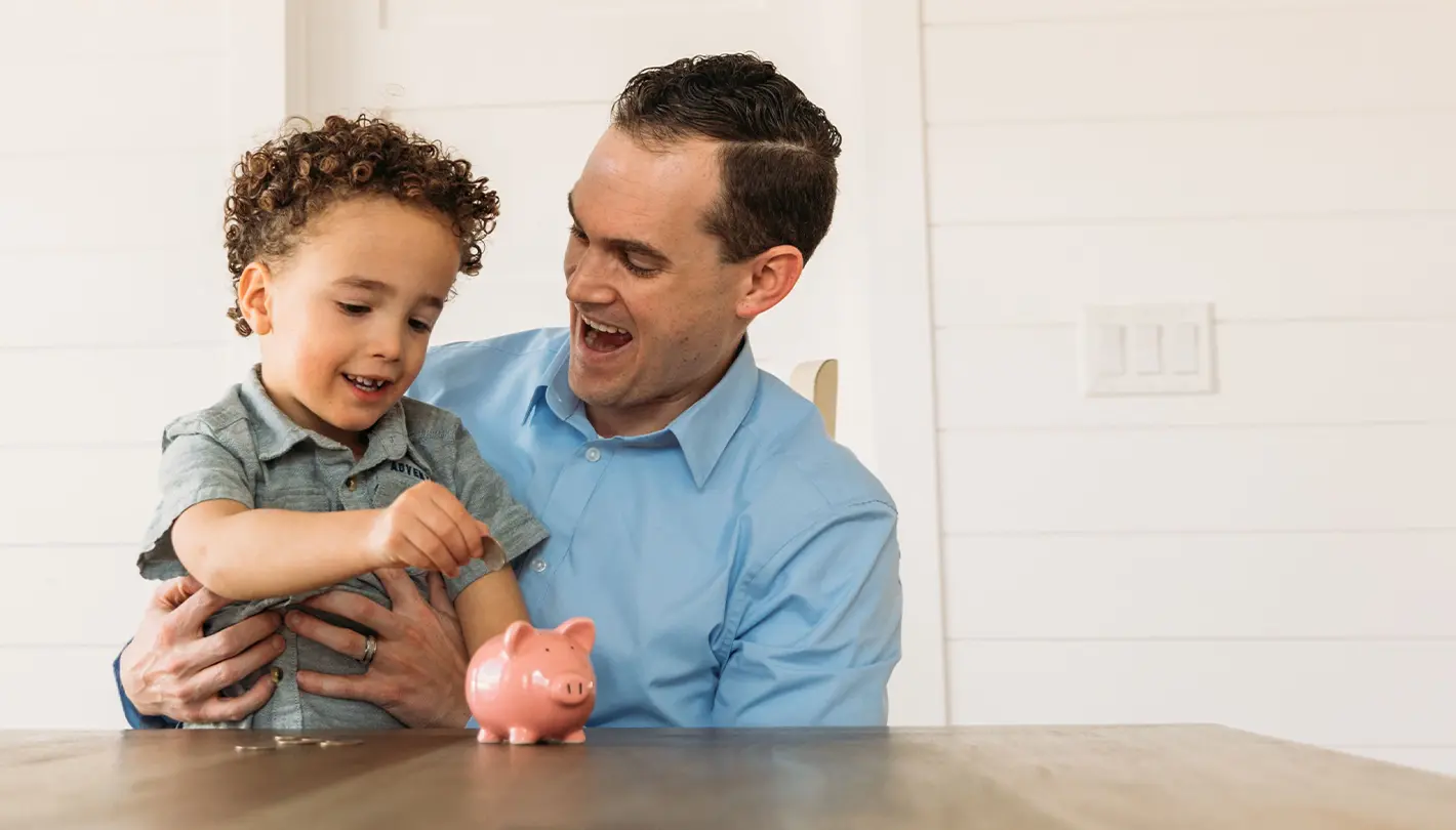 Father and child putting coins into a piggy bank talking about how money grows